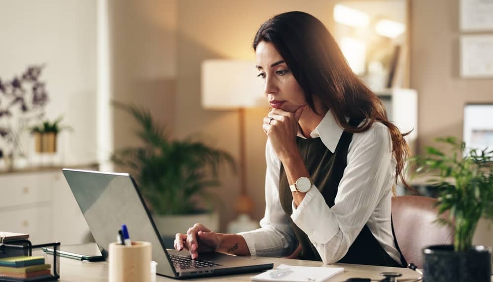 Professional woman researching plastic surgery website copywriting services on laptop computer in modern office setting