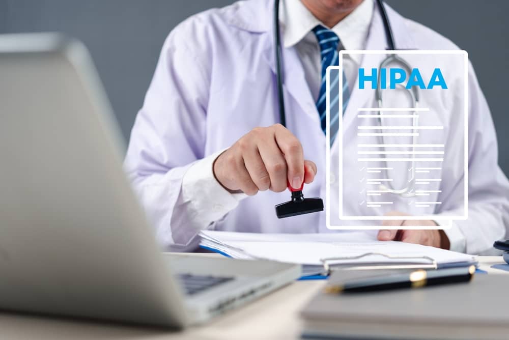 Healthcare professional in white coat and stethoscope stamping HIPAA compliance document with official seal at medical office desk