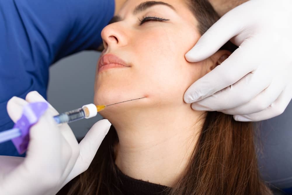 Medical professional performing non-surgical jawline contouring with hyaluronic acid dermal filler using 7-layer safety protocol for lower face enhancement