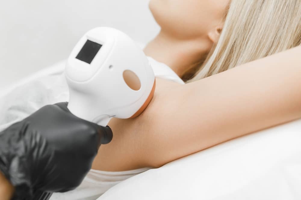 Laser hair removal handpiece being applied to patient's underarm area during professional treatment