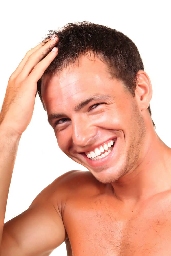 Confident young man with thick healthy hair smiling and running hand through hair after successful PRP hair restoration treatment