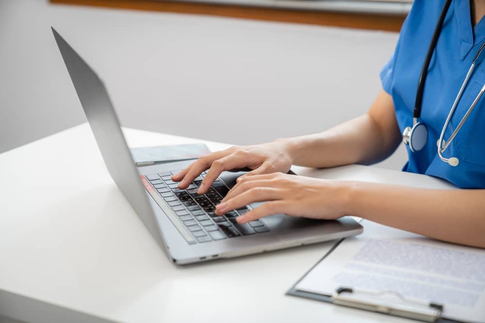 Registered nurse with stethoscope typing on laptop creating clinical copywriting content for medical spa marketing
