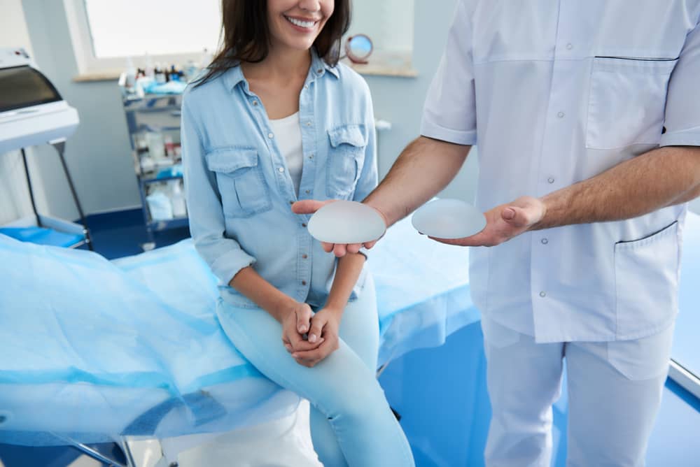 Smiling female patient in consultation with plastic surgeon discussing breast implant options in modern medical office, showing the premium patient experience and trust that elite practices deliver