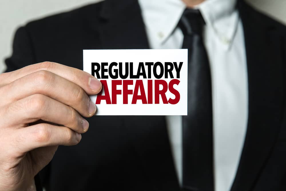 Professional in business suit holding Regulatory Affairs card - medical aesthetics compliance expertise