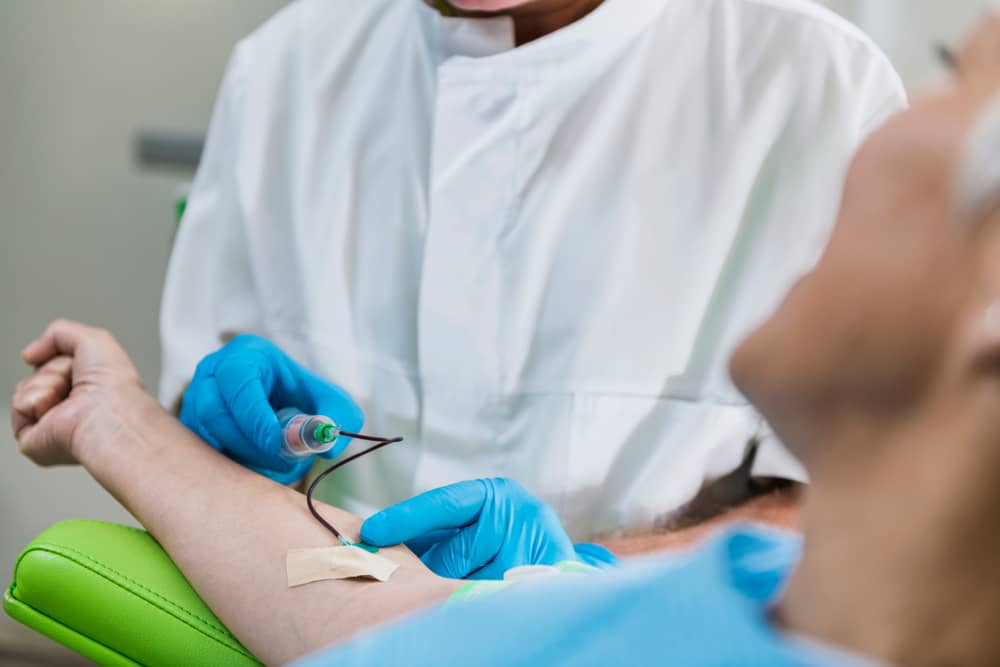 Medical professional in white coat drawing blood from patient's arm for PRP hair loss treatment preparation in clinical setting