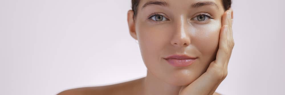Woman with flawless, dewy skin gently touching her cheek, showcasing natural radiance and smooth complexion