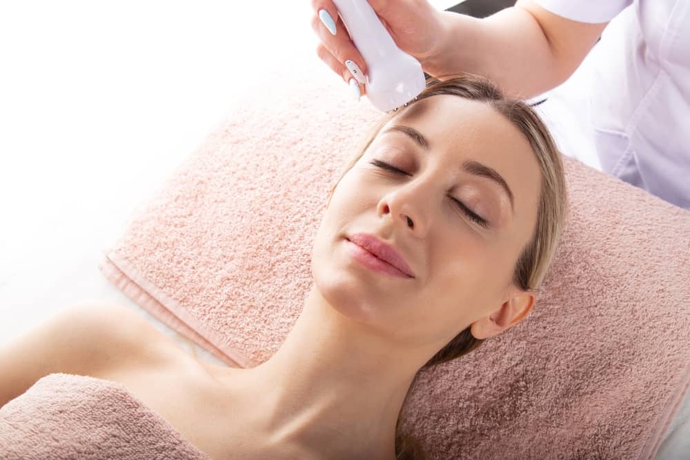 Professional aesthetician performing HydraFacial treatment with device on relaxed woman's face at med spa