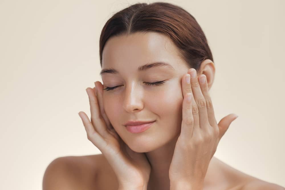 Woman gently touching her smooth, glowing facial skin with both hands after HydraFacial treatment
