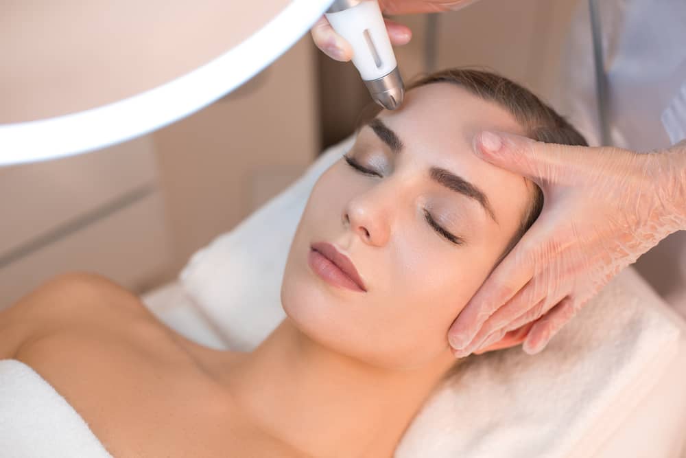Medical aesthetician performing RF microneedling facial treatment on young woman at modern med spa