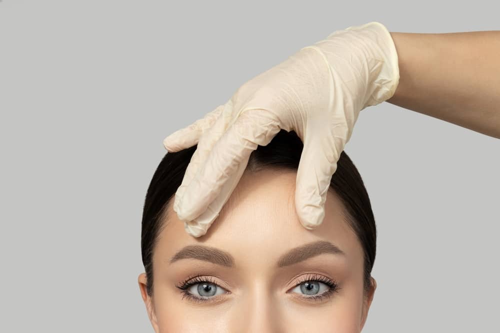 Medical professional in white gloves examining young patient's forehead for cosmetic treatment assessment