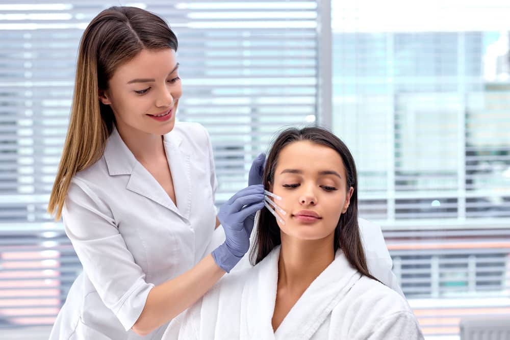 Medical aesthetician performing facial injection treatment on young woman patient at modern med spa clinic