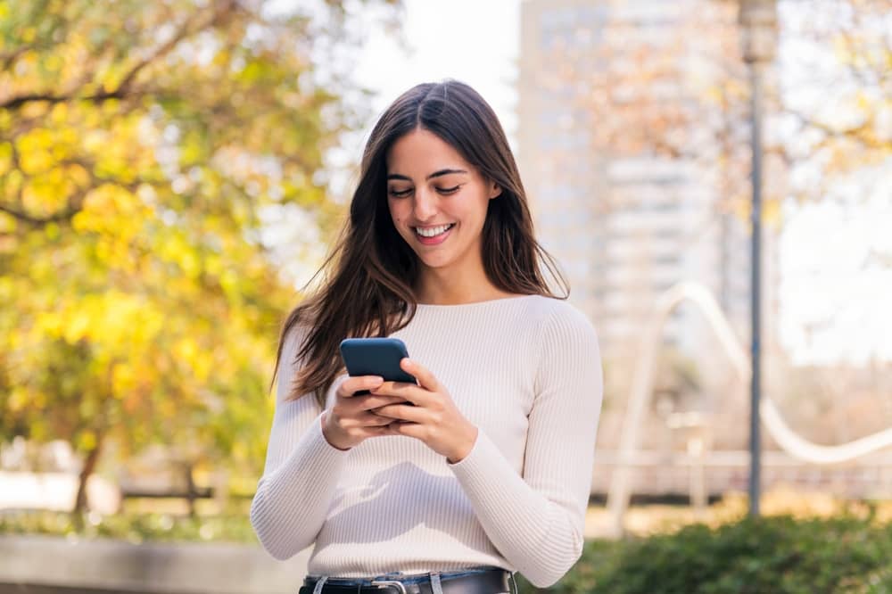 Young millennial woman smiling at smartphone researching aesthetic treatments on social media