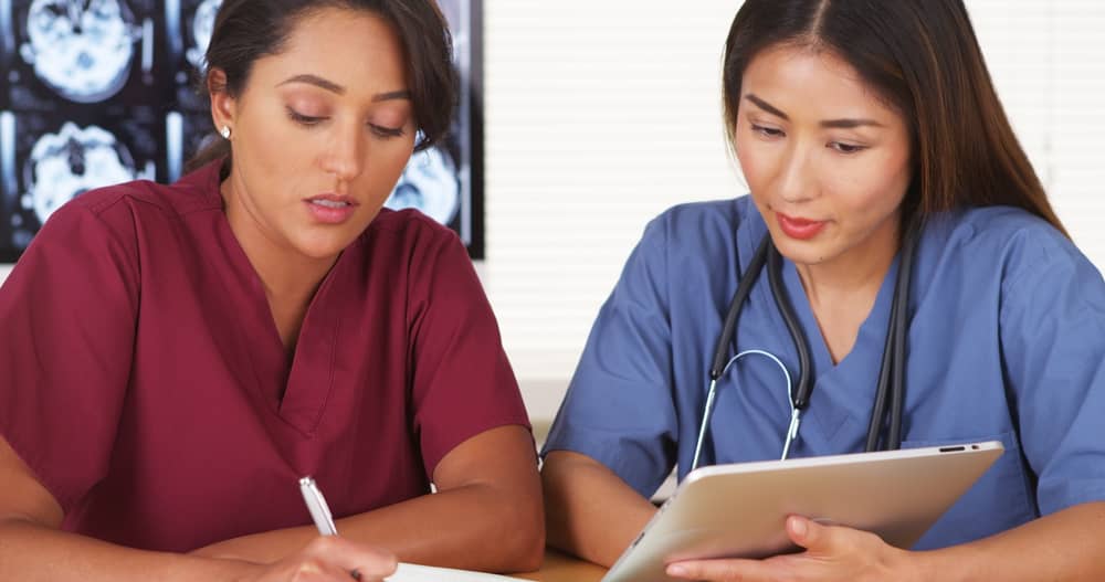 Two nurses in scrubs reviewing content together on a tablet