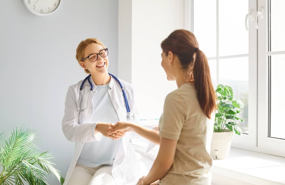 Healthcare provider in white coat warmly shaking hands with patient in bright clinical setting
