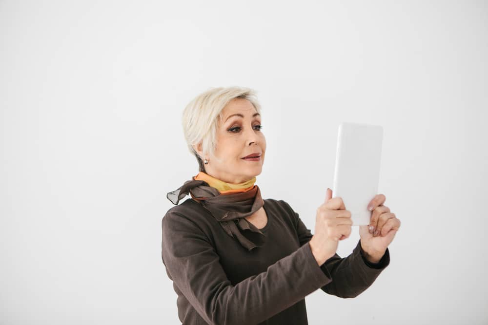 Mature woman in black outfit and colorful scarf looking at tablet device against white background