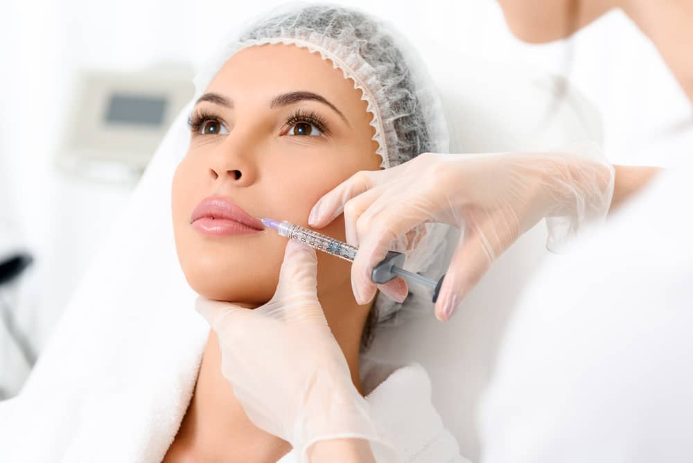 Woman receiving lip filler injection from aesthetician wearing gloves in a med spa setting