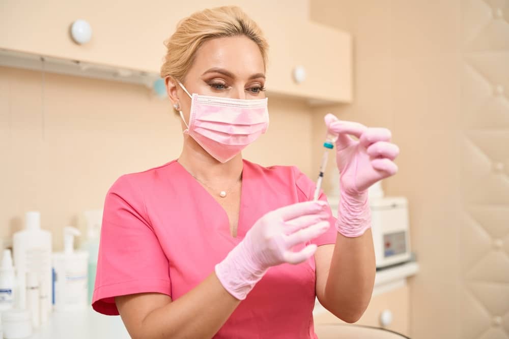 Aesthetic injector in pink scrubs and mask preparing syringe for treatment in med spa clinic
